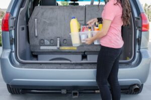 Woman grabbing cleaning supplies from car.