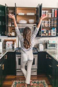 Woman standing in front of open kitchen cabinets.