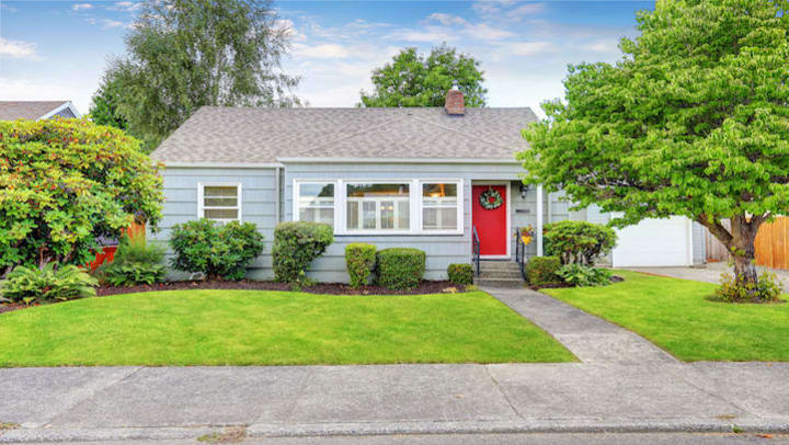 A small, blue house with a red door and landscaped yard.