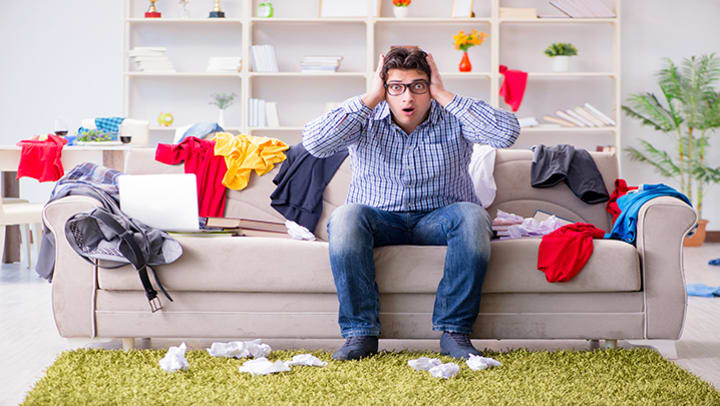 Stressed man sitting on a couch in a messy room.