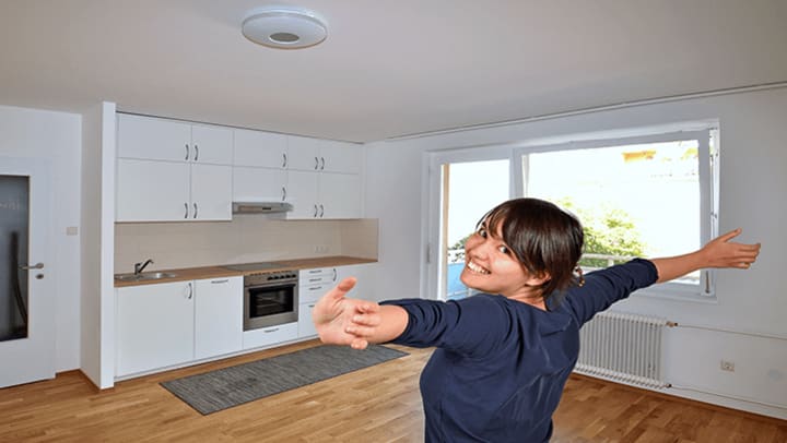 A woman smiling in an empty kitchen with her arms stretched out.