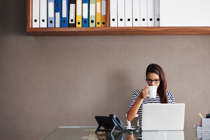 A woman sipping coffee at a desk.