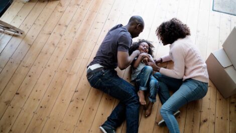 A family laughing and lying on a hardwood floor.