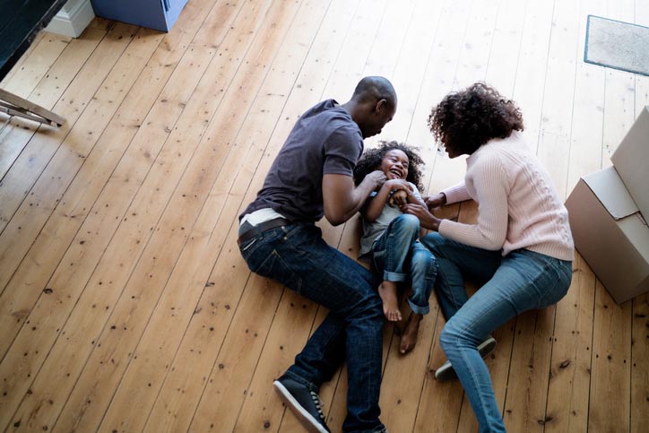 A family laughing and lying on a hardwood floor.