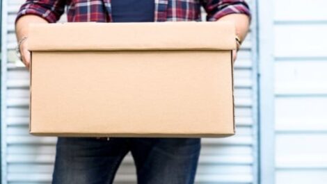 A man holding a moving box in front of a storage unit.