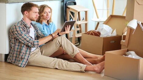 A couple looking at a tablet surrounded by moving boxes.