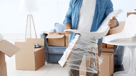 A man wrapping up a chair surrounded by moving boxes.