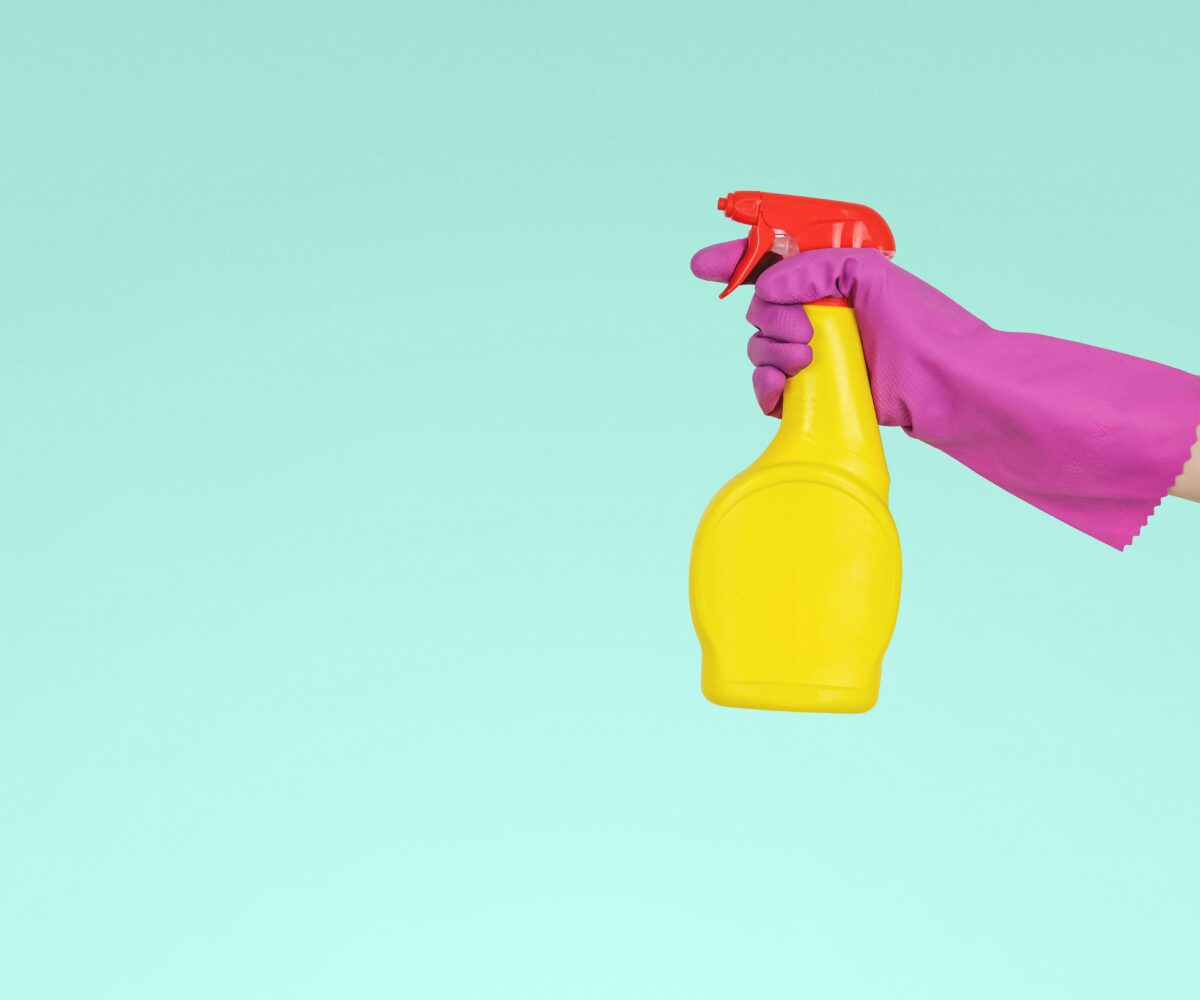 Person wearing gloves holding cleaning spray bottle.