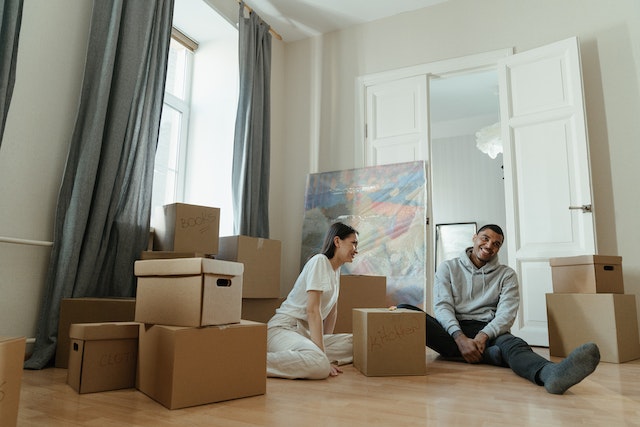 Man and woman sitting on a floor surrounded by cardboard boxes while preparing for a long distance move