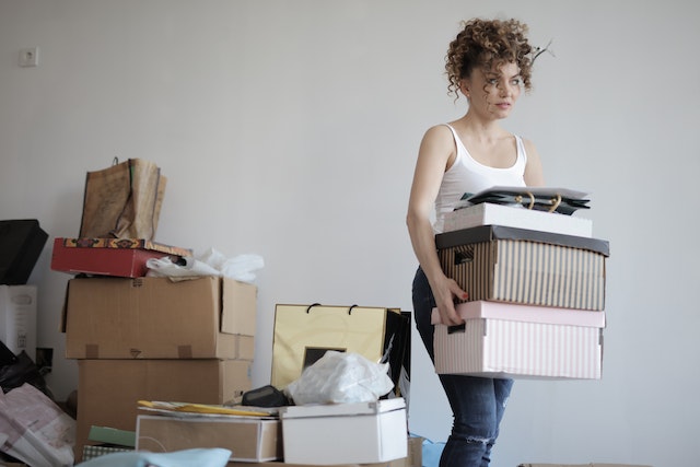 Woman decluttering and carrying a pile of boxes while moving away from another pile of boxes